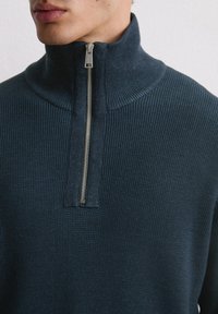 Dunkelblauer, gerippter Strickpullover mit hohem Kragen und halbem Reißverschluss; verfügt über einen glatten Reißverschluss und einen strukturierten Stoff.