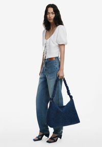 White puff-sleeve top with lace-up detail, paired with light blue high-waisted jeans. Carrying a large dark blue bag with embossed floral design.