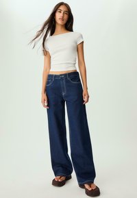 Svetlo siva rebrasta kratka majica u kombinaciji s tamnoplavim širokim trapericama. Outfit ima prilagođen siluet i meke materijale.