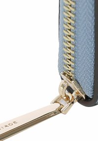 Lyseblå tekstilpung med guld lynlås, der har et metallic hardware-fixeringspunkt og glatte læderkanter.