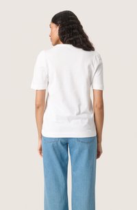 Witte T-shirt met korte mouwen en een rechte zoom, gecombineerd met lichtblauwe high-waisted jeans. Eenvoudig ontwerp, gladde katoenen textuur.