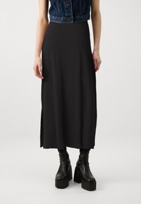 Sort, ankel-langt nederdel med en glat tekstur og sideslids, parret med en cropped denimvest og chunky hælede sorte støvler.