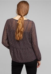 Blusa nera trasparente con piccolo motivo floreale bianco e rosso, vita elasticizzata e maniche lunghe. Tessuto morbido con una vestibilità comoda.