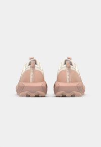 Zapatillas de entrenamiento en rosa claro y crema con una parte superior de tela texturizada, suela de goma gruesa y tiradores en el talón para ponerlas y quitarlas fácilmente.