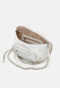 Weißes Handtaschen mit strukturiertem Oberflächen, silberner Kettenriemen, mehreren Reißverschlusstaschen und funkelnden Akzenten. Futter in Beige mit Logomuster.