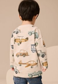 Sudadera beige clara con estampados de vehículos coloridos, que incluyen coches y aviones, con mangas largas y cuello acanalado.