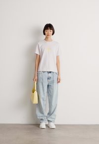 Hvit t-skjorte med korte ermer og trykt gul tekst, kombinert med lyseblå høytlivsjeans og en gul håndveske. Hvide joggesko.