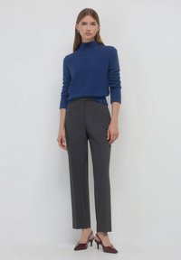 Blauer Rollkragenpullover aus strukturiertem Strick, kombiniert mit grauen Tailored-Hosen und bordeauxroten High-Heels. Einfaches und modernes Design.