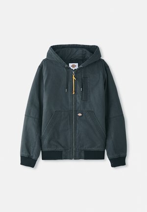 Jachetă cu fermoar, cu glugă, de culoare neagră, fabricată din material de canavas. Prezintă manșete ribbate, două buzunare frontale și detalii discrete de cusătură. Fermuar cu un detaliu de accent.