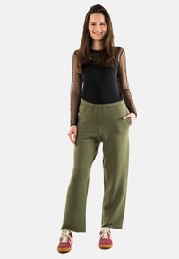 Top negro de manga larga con malla de lunares y pantalones verdes de corte holgado. Combinado con zapatillas deportivas rosas y blancas, que cuentan con una cinturilla elástica.