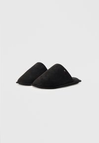 Zapatillas de ante negras con un diseño puntiagudo y un suave forro interior. Presentan un pequeño logo como acento en el costado. Superficie superior texturizada.