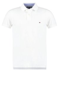Polo blanc à manches courtes avec col, deux boutons et petit logo rouge, blanc et bleu sur le côté gauche de la poitrine.