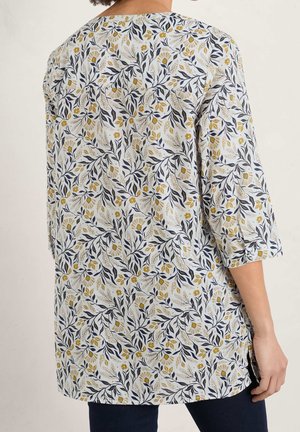 Túnica floral con mangas tres cuartos, presenta una base blanca, hojas azul marino y acentos florales amarillos, confeccionada con tela ligera.