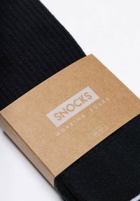 Czarne skarpetki ribbed zapakowane z brązową tekturową etykietą. Etykieta zawiera nazwę marki "SNOCKS" oraz napis "SKARPETKI ROBOCZE" w białym tekście.
