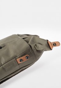 Borsa verde oliva realizzata in materiale resistente, con un design pieghevole, dettagli in pelle marrone e accessori in metallo con rivetti.