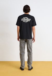 Černé bavlněné tričko s velkým bílým logem "Dickies" na zádech. Kombinováno s vybledlými šedými džíny a černými nazouvacími botami.