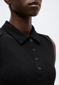 Κοντινό πλάνο ενός ατόμου που φοράει μαύρο πικέ πόλο χωρίς μανίκια με τέσσερα μαύρα κουμπιά και διπλωμένο γιακά.