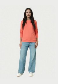 Koronkowy sweter z długimi rękawami, zestawiony z jasnoniebieskimi spodniami o szerokich nogawkach i białymi butami, na neutralnym tle.