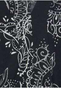 Schwarzer Stoff mit aufwendigen weißen Blumen- und Wirbelmustern. Sichtbares V-Ausschnitt-Design und feine Stricktextur.