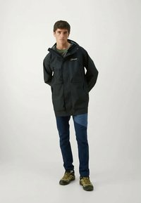 Αδιάβροχο μαύρο μπουφάν με κουκούλα, δύο μπροστινές τσέπες και κλείσιμο με φερμουάρ. Συνδυάζεται με μπλε και σκούρο μπλε τζιν και καφέ ορειβατικά παπούτσια.