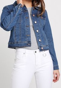 Modrá džínová bunda s krátkým střihem, s knoflíkovým zapínáním a náprsními kapsami; má kontrastní švy a měděné ozdobné prvky.