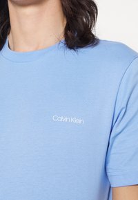Jasnoniebieska bawełniana koszulka z okrągłym dekoltem i krótkimi rękawami. Na lewej piersi małe białe logo "Calvin Klein".