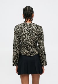 Chaqueta con estampado de cebra en tela beige y negra, con mangas largas y diseño ajustado. Se lleva con una falda negra plisada.