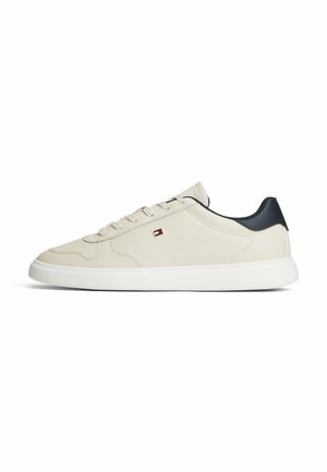 Baskets basses beige avec semelle blanche, talon bleu marine, lacets beige et petit logo rectangulaire sur le côté.