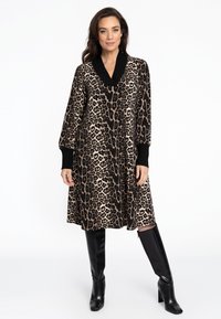 Leopardenmusterkleid mit einem schwarzen V-Ausschnitt und gekrempelten Ärmeln, knielang, kombiniert mit glänzenden schwarzen Stiefeln bis zum Knie.