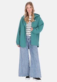 Türkiz vízálló dzseki kapucnival, fehér és tengerészkék csíkos ing, bő szárú világoskék farmer, fekete tornacipők. Rugalmas mandzsetták és húzózsinór jellemzi.