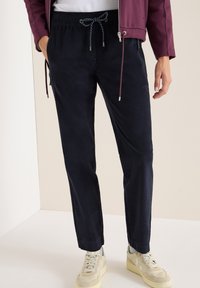 Granatowe chinosy o luźnym kroju, z elastycznym paskiem z troczkiem oraz bocznymi kieszeniami, połączone z jasnobeżowymi sneakersami.