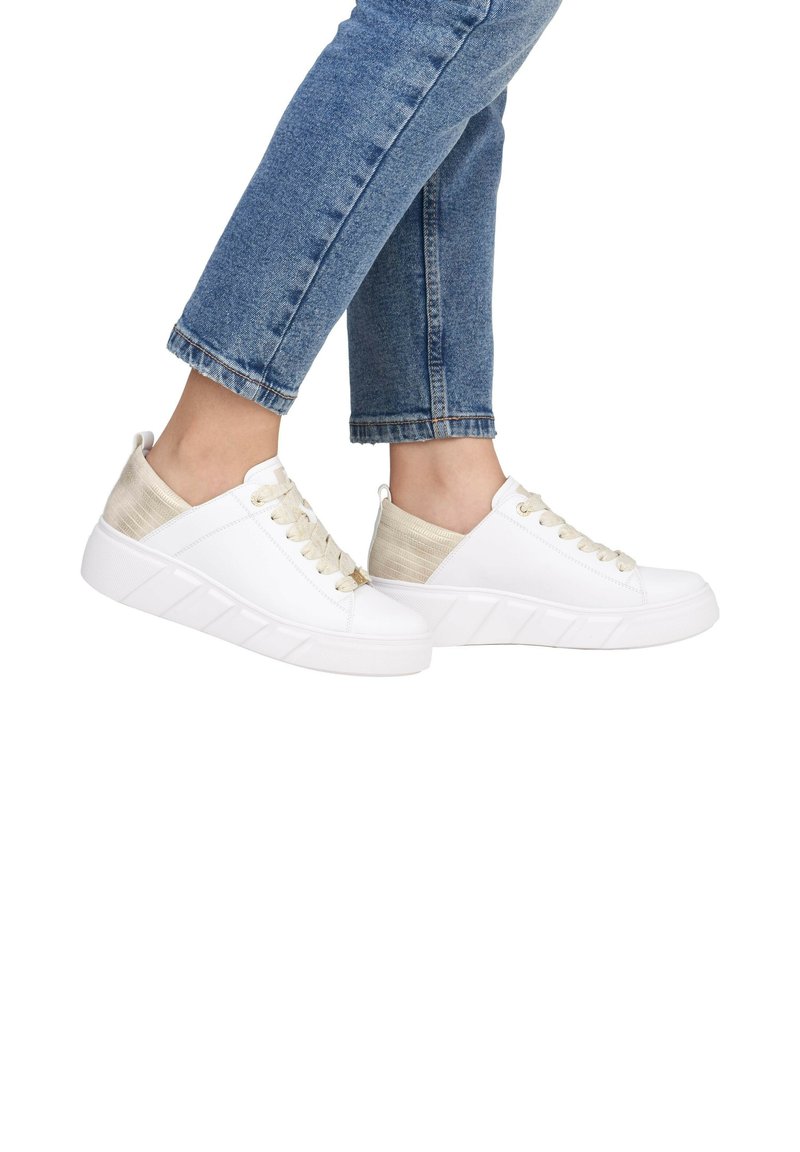 Baskets blanches avec des accents beiges texturés, à bout rond, semelle en caoutchouc plate et lacets dorés, associées à un jean en denim bleu retroussé.