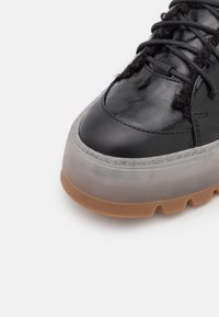 Baskets noires avec une tige brillante et des lacets texturés. Dotées d'une semelle semi-transparente et d'une semelle extérieure couleur gomme pour une meilleure traction.