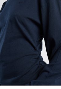 Navy blue fitted top with long sleeves, featuring ruched detailing at the side. Made from smooth, stretchy cotton material.