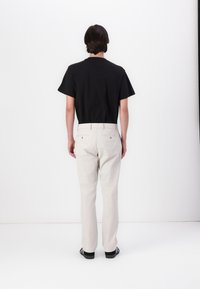 T-shirt noir à manches courtes avec un col arrondi, associé à un pantalon beige clair. Le modèle est de dos, portant des baskets noires. Tissu texturé.