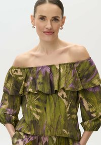 Blusa off-the-shoulder en estampado floral verde y morado, con acentos de volantes, tela suave y mangas tres cuartos.