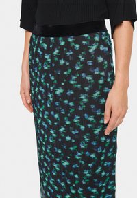 Jupe noire avec un motif floral vert et bleu, dotée d'un design plissé et d'une taille en velours. La texture semble lisse et fluide.
