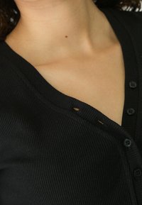 Czarny cardigan z prążkowanej tkaniny o dekolcie w kształcie litery V, z czarnymi guzikami i małym otwarciem przy dekolcie. Miękka tekstura i dopasowany fason.