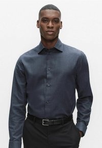 Mørkeblå ternet skjorte med knaplukning på kraven, lange ærmer og en glat tekstur. Kombineret med sorte bukser og et sort bælte.