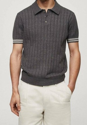 Man draagt een donkergrijs kortarmig polohemd met verticale strepen en witte streepaccenten op de mouwen, gecombineerd met lichtbeige broek.
