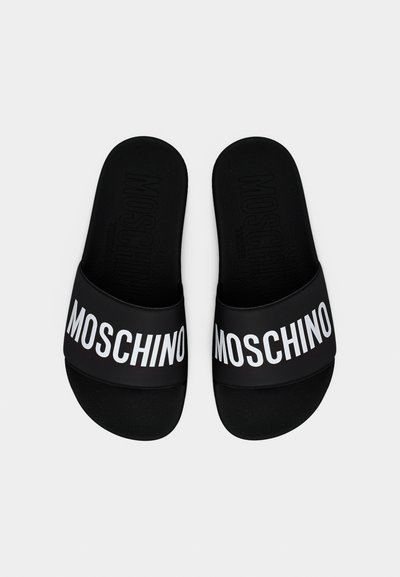 Μαύρα σανδάλια με πλατφόρμα και φαρδιές λουριά με έντονο λευκό λογότυπο "MOSCHINO" σε κάθε λουρί, από πάνω σε λευκό φόντο.
