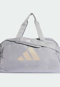 Vaaleanharmaa, mattapintainen duffel-laukku, jossa suuri kermanvärinen logo ja etuosan alaosassa perforoidut yksityiskohdat. Säädettävät hihnat.