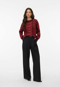 Pull en tricot rouge avec un motif textuel "AMOR" et "LOVE", associé à un pantalon noir taille haute. Le pull présente une coupe décontractée et des poignets côtelés.