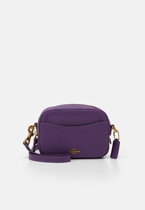 Sac bandoulière en cuir violet avec poche avant, ferrures dorées, fermeture éclair et une étiquette en cuir assortie sur une sangle amovible.