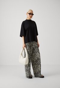 T-shirt noir oversize, pantalon large à motifs avec un design en peau de serpent, et un sac à main en forme de croissant blanc. Les accessoires incluent des lunettes de soleil.