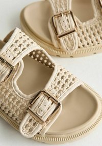 Sandalias beige con parte superior de sintético tejido, dos hebillas ajustables en metal en tono dorado y suela de goma acolchada para mayor comodidad.