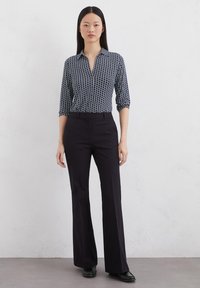 Hemd mit Marine-Muster und drei Viertelärmeln, kombiniert mit schwarzer ausgestellter Hose. Beide Kleidungsstücke haben eine glatte Textur und einen taillierten Schnitt.