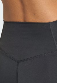 Leggings da palestra neri a vita alta realizzati in materiale elastico con cuciture flatlock e una texture liscia e opaca. Presentano un design sagomato.