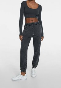 Donkergrijze cropped lange mouwen rib top gecombineerd met bijpassende joggingbroek met trekkoord, voorzien van elastische boorden en witte sportschoenen.