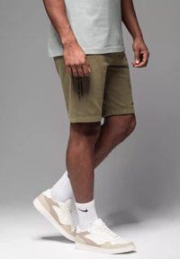 Shorts kaki avec une finition texturée, poches sur les coutures latérales et détails imprimés. Associés à des chaussettes blanches et des baskets beiges.